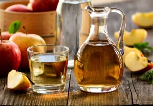 Pitcher and glass full of vinegar on a table next to sliced apples