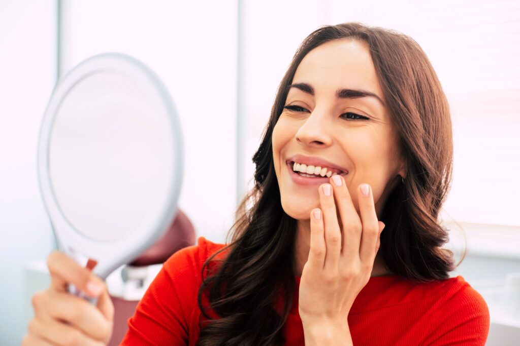 Woman in red shirt admiring her smile in handheld mirror